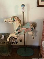 Full view of the wooden carousel horse mounted on metal pole and round base, showing the horse in a galloping pose with floral design.