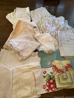 Photo showing folded white, cream, beige, and floral linens in various sizes including tablecloths and napkins