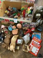 Wide view of the lot showing boxed craft kits, assorted dolls, plush toys, and small toys packed in a cardboard box and arranged on floor.