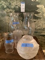 Five assorted glass lamp shades including a frosted floral globe, two tall etched chimneys, and two clear cut glass shades
