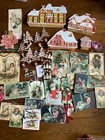 Full view of lot displaying Victorian-style paper decorations including house cutouts, snow-covered trees, snowmen, Victorian holiday cards, and ornaments