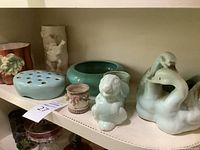 Shelf display showing light blue flower frog, green Bauer bowl, and two light green swan figurines.