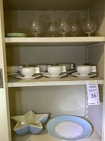 Shelving with various glassware including stemmed glasses and ceramic cups with saucers, star-shaped dish and decorative plate