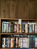 Two wooden shelves with approximately 40 VHS tapes and DVDs of various movies and shows, including Disney and family titles.