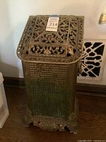 Front and left side view of tall rectangular ornate metal container with decorative pierced lid and detailed feet.