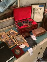Photo showing arrangement of a wooden keepsake box with rosaries, medals, a framed quote, several framed religious prints, prayer books and keepsake boxes on a dresser.