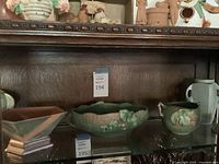 Glass-shelf view showing hexagonal bowl on the left, scalloped-edge oval planter in center, and small handled jug on right.