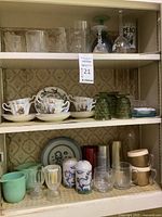 Cabinet shelf showing assorted clear glassware including drinking glasses and decorative glass pieces.