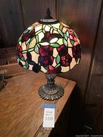 Full view of table lamp showing stained glass shade with floral patterns and metal base on wooden table.