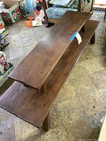 Two-tier wooden bench or display table from a side angle, showing medium brown wooden finish with visible grain and two tier height difference.