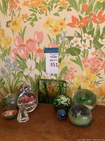 Nine art glass items displayed against floral wallpaper