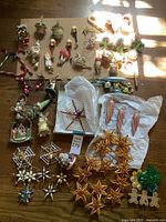 Full lot overview with assortment of vintage Christmas ornaments spread on wood surface showing candy canes, star clusters, basket floral arrangements, and small figurines.