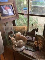 Photo showing ceramic squirrel figurine, dark carved horse figurine, framed picture of cats, and religious plaque.