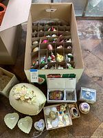 Overall view of the lot including box with assorted small ornaments, decorative eggs, floral centerpiece egg and heart dishes