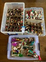 Three plastic storage bins with cardboard dividers containing over fifty assorted glass ornaments on a tabletop