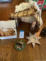 Wide view of lot showing large rustic nativity stable, carved wooden figurines in box, decorative star ornament and small ceramic nativity display on a wooden table