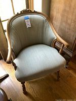 Front and side view of vintage armchair showing curved wood arms, turned legs, and grey fabric upholstery.