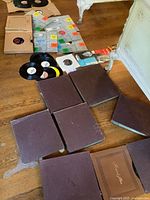 Over 20 vintage vinyl records and albums in mixed sizes laid out on wooden floor including original sleeves and binders.