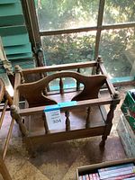 Front and top angled view of wooden magazine rack showing spindle side supports, carry handle, and drawer below.