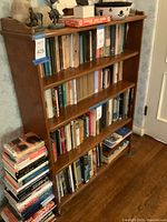 Full side and partial front view of the wooden bookshelf showing four shelves, filled with books and some decorative items on top.