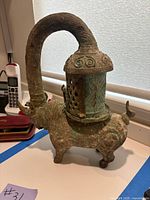 Side angle view of antique bronze ox-shaped candle holder showing handle and lantern holder on back.