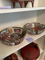 Two porcelain bowls displayed side by side on shelf; one round, one scalloped.