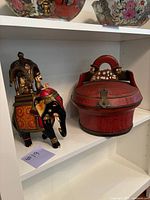Antique Chinese wedding basket and hand-painted elephant statue displayed together on a white shelf.