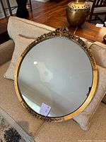 Full view of the gold oval mirror resting on couch.