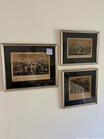 Three framed antique historical black and white prints mounted together on a white wall. Prints have beige mats with black backgrounds and gold-trim frames.