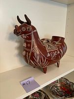 Full view of red and white hand-painted Peruvian pottery cow/bull sculpture on shelf