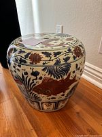 Full view of the cylindrical porcelain garden stool decorated with koi fish and floral designs on a wooden floor beside a wall outlet.