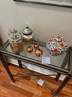 Overview of seven containers displayed on glass surface including three mercury glass lidded containers, three hammered copper containers, and one colorful porcelain vase.
