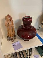 Both antique statue and burgundy pot displayed together on a white shelf, showing detailed features of both items.