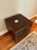 Square antique wooden trunk chest showing front and top sides with metal rivet detailing and a lockable latch.