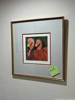 Framed art piece hung on wall depicting two pink flamingos in a decorative gold frame.