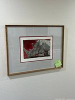 Front view of the framed rhino art print with gold-colored ornate frame hung on a wall.