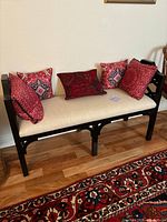 Front view of wooden bench with beige upholstered seat and 5 red patterned cushions, showcasing lattice work on sides and floor rug underneath