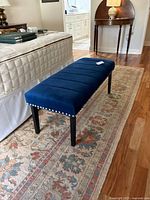 Side angle of the blue velvet cushioned bed bench showing stud detailing and leg design.