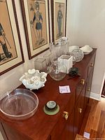 Photo of assorted clear glass and crystal bowls, vases, and decorative items on wooden cabinet