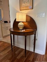 Full frontal photo of the flip top vintage wood table with lamp on top. Shows semi-circular shape and tapered legs.