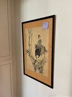 Framed antique Asian art piece mounted on an orange mat in a black frame, hanging on a wall, angle view