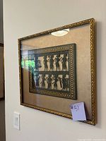 Framed art showing two rows of black 3D silhouette figures set on a beige background with decorative patterned inner border.