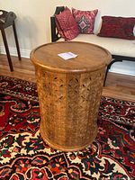 Round carved wooden table with floral patterns, showing overall top and side view on colorful rug.