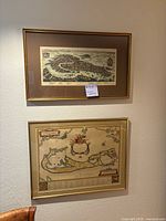 Both framed maps hanging on a wall showing top aerial city map and lower nautical chart style map with gold frames.