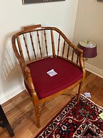 Front view of mid-century style bamboo-inspired wooden chair with red cushion seat on wooden floor, next to lamp and carpet.