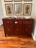 Frontal view of the mid-century wood cabinet credenza showing the three drawers and three cabinet doors with gold-tone ring handles and various glassware on top.