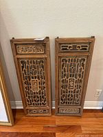 Two standing antique wooden Chinese doors with carved lattice and floral patterns visible against a white wall and hardwood floor.