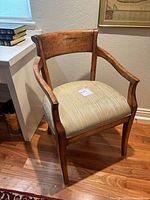View of the full front and side of the vintage wooden chair showing curved arms, upholstered seat, and patina on wood finish.