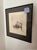 Framed artwork featuring a boy playing a flute while riding a water buffalo, with calligraphy and red stamps on the side.