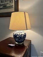 Full view of the lamp turned on, showing the porcelain base with blue floral design and beige shade.